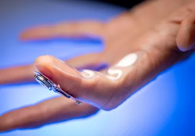 A finger wearing the sweat-sensing device is shown against a bright blue background.