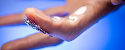 A finger wearing the sweat-sensing device is shown against a bright blue background.