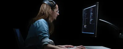 A person sits in front of a computer with electrodes attached on their head, signifying brain-computer interface devices.