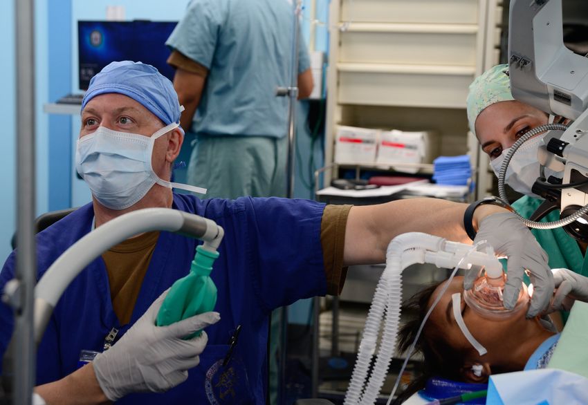 An anesthesiologist holds a mask over a patient’s nose and mouth to administer them anesthesia for a surgery.
