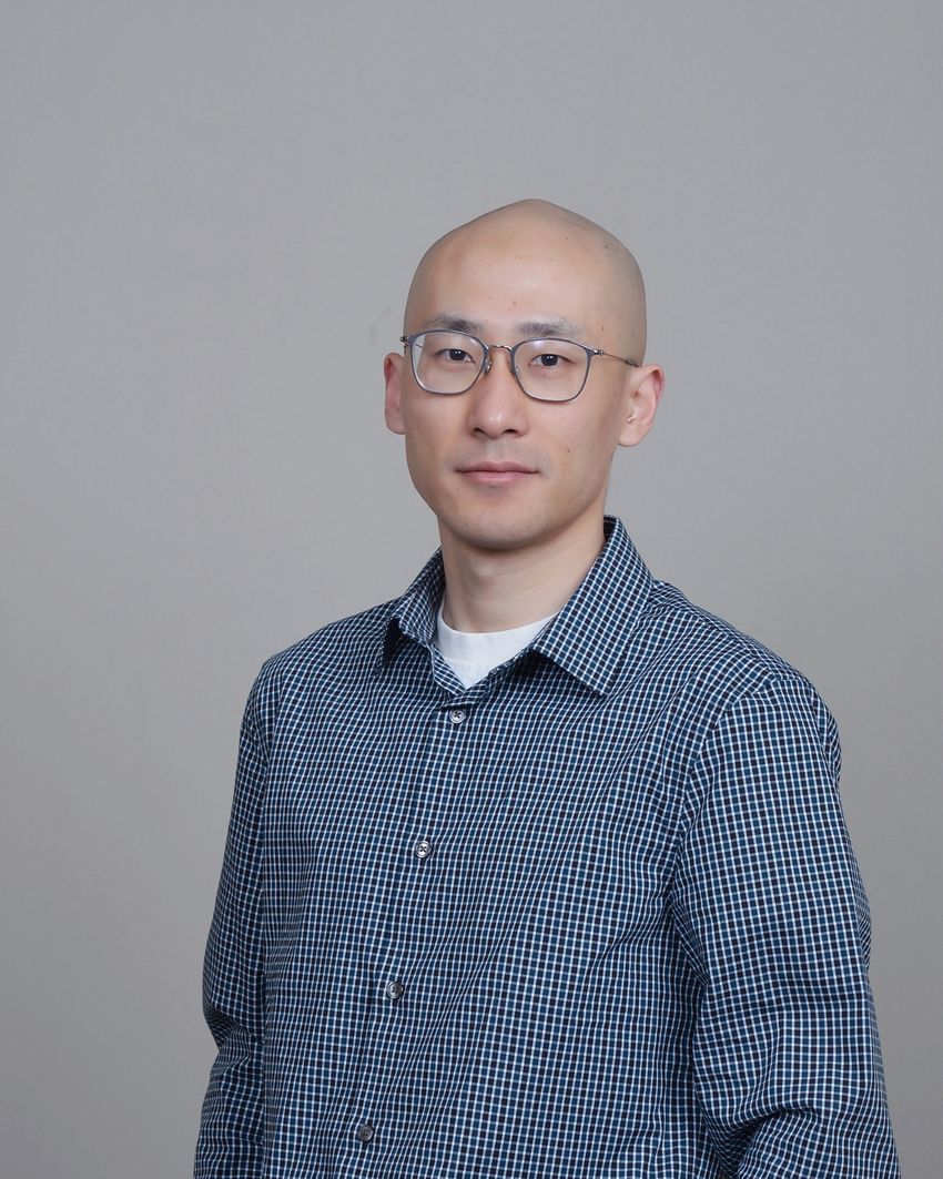 Portrait photo of Guangyuan Li against a gray background. Li is wearing a blue and white checkered shirt and has glasses. Portrait photo of Guangyuan Li against a gray background. Li is wearing a blue and white checkered shirt and has glasses.