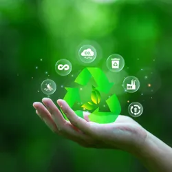 Photograph of a person’s hand raised against a background with green, leafy trees. There are icons representing concepts of recycling, reducing carbon dioxide, and reusing materials floating above the hand. 