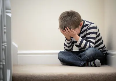 Image of a young boy sitting on the staircase. He has his head in his hands.