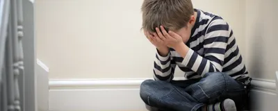 Image of a young boy sitting on the staircase. He has his head in his hands.