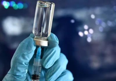 A blue-gloved hand inserts a syringe into a vaccine vial.