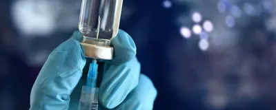 A blue-gloved hand inserts a syringe into a vaccine vial.