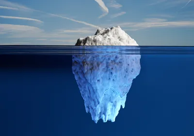 Image of a white iceberg exposing a small part out of water and hiding mostly under the ocean.