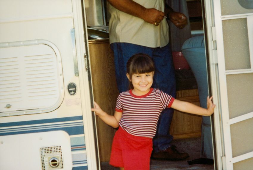 A photograph of a young Savannah wearing a red striped top and red skirt standing at a door. A photograph of a young Savannah wearing a red striped top and red skirt standing at a door.