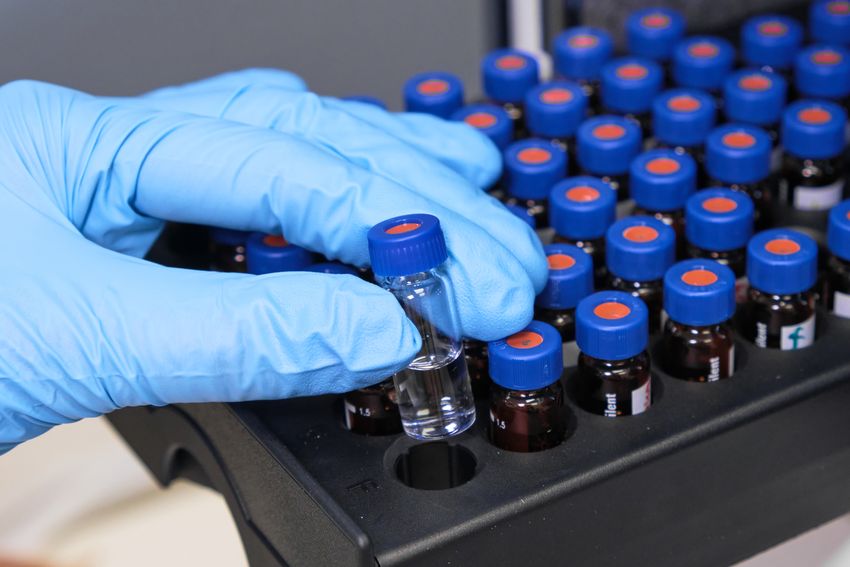 A photo of a researcher placing a glass vial into the tray of a high-performance liquid chromatography autosampler. A photo of a researcher placing a glass vial into the tray of a high-performance liquid chromatography autosampler.