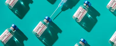 Vials of the coronavirus vaccine with the syringe is shown against an aqua background.