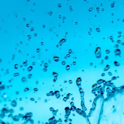 Abstract macro photography of pure water droplets and splashes suspended against a bright blue background