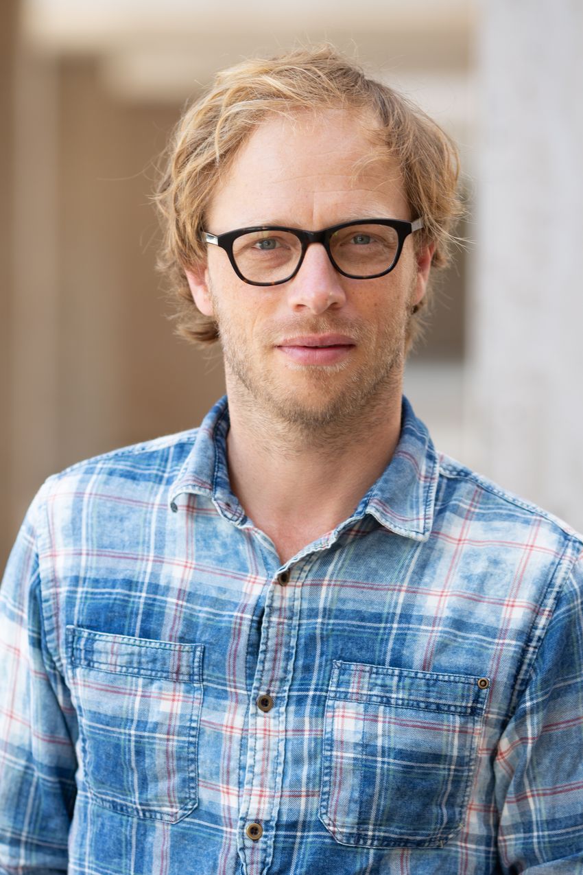 Sam Van de Velde is wearing black-framed glasses and a blue plaid button-down shirt.