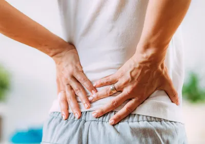 Image of a woman with nerve pain in her lower back. She touches her lower back with both hands.