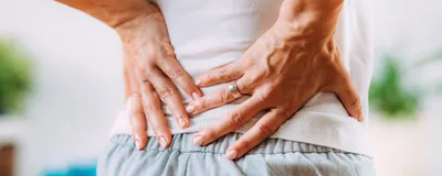 Image of a woman with nerve pain in her lower back. She touches her lower back with both hands.
