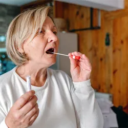 A person swabs her mouth for saliva, signifying a saliva-based age prediction test.