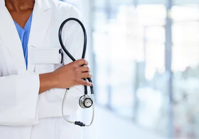 A doctor holds a stethoscope in her hands with her arms crossed.