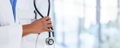 A doctor holds a stethoscope in her hands with her arms crossed.
