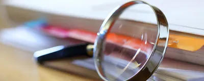 A magnifying glass, representing increased scrutiny into this student’s publication record, leans against a stack of papers.