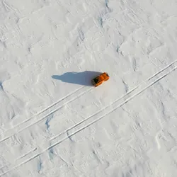 An orange car drives through the snow on the arctic tundra. Two sets of vehicle tracks are shown, representing a pivot from one career path to another.