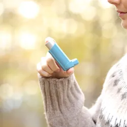 Woman hand holding asthma inhaler, signifying adult women being more prone to allergies.