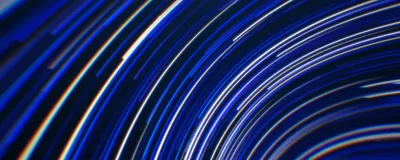 Concentric blue and white light trails curving across a dark field, evoking sustained high-speed rotation