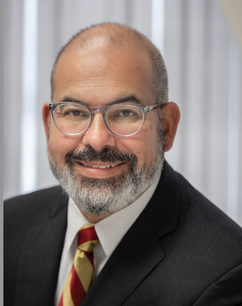 Jorge Nieva smiles, wearing a white shirt, black jacket, glasses, and a red-and-yellow tie against a white backdrop. Jorge Nieva smiles, wearing a white shirt, black jacket, glasses, and a red-and-yellow tie against a white backdrop.