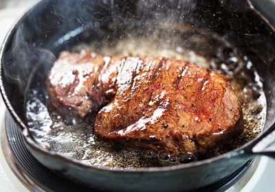 A steak frying in a pan.