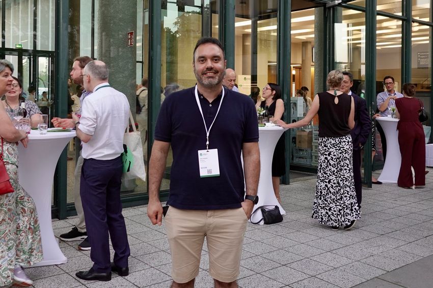 A man smiles for a photo outside of a university.