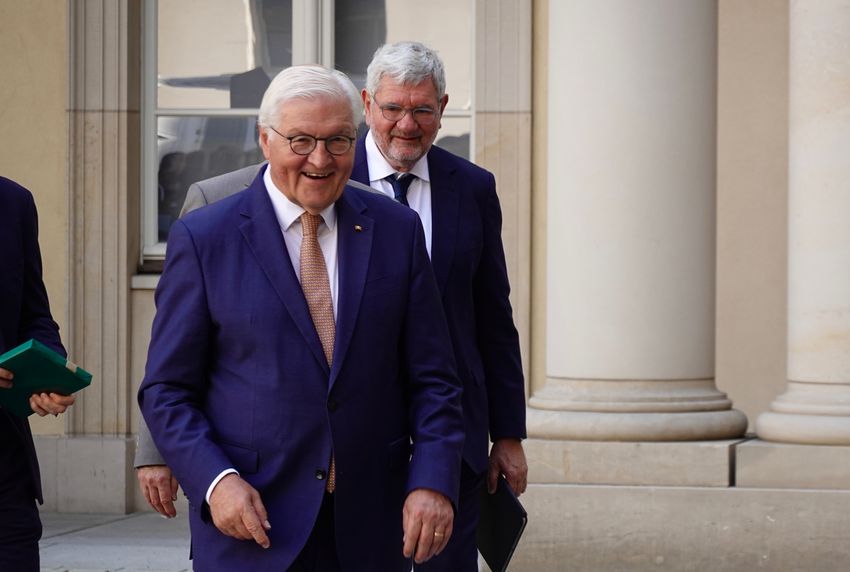 A man smiles while walking. Another man is walking behind him.