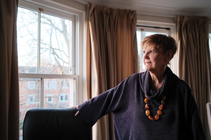 Dorothy Bishop wears a dark sweater and brown necklace while looking out the window.