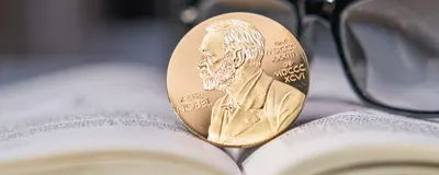 Image of a Nobel Prize coin on an open book with glasses in the background.