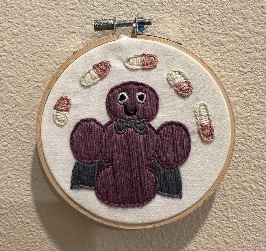 Image of an embroidered microbe. It wears a cape and is surrounded by antibiotics. Image of an embroidered microbe. It wears a cape and is surrounded by antibiotics.