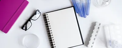 Image of table with various laboratory items: a notebook, glasses, flasks, and vials with liquid.