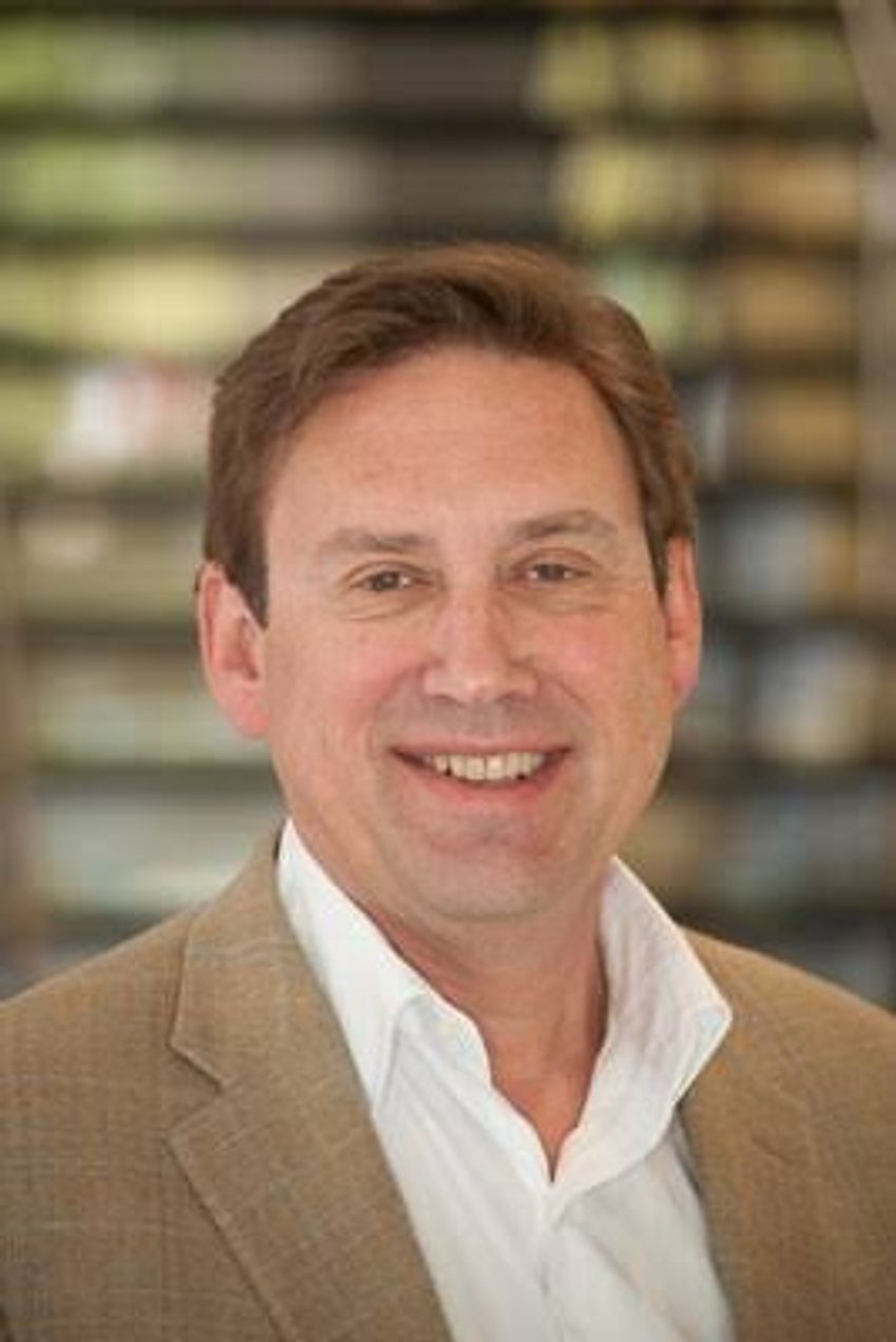 Bradley Perkins wears a cream colored blazer and white shirt in a headshot photo.