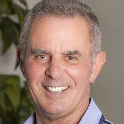 Photo of a middle-aged man with short, gray hair and hazel eyes. He has a small earring in one ear and is smiling at the camera.