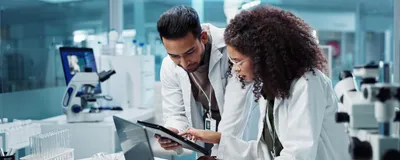 Two people, one a clinical trial monitor, discuss clinical trial needs in a laboratory setting.