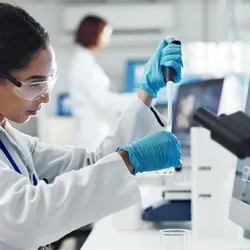 A scientist pipetting a small-volume biological sample in an analytical laboratory, with mass spectrometry data visible on a monitor, illustrating biopharmaceutical characterization workflows for AAV analytics and viral vector quantification.