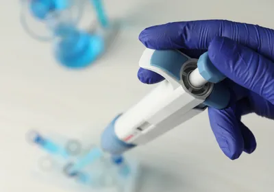 Gloved hand operating a manual micropipette in a laboratory.