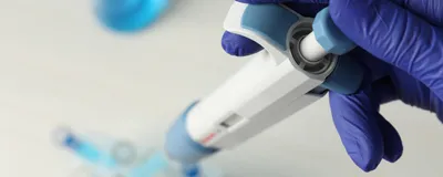 Gloved hand operating a manual micropipette in a laboratory.