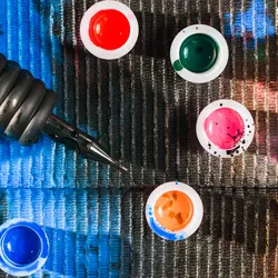 A tattoo machine sits on a dark background next to pots of colorful tattoo ink.
